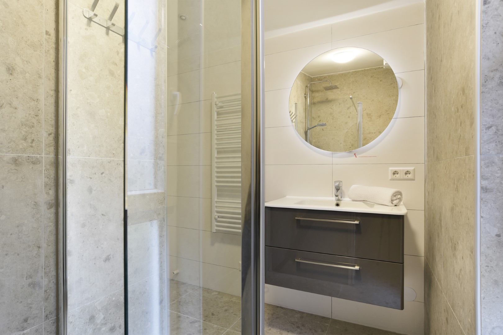 De stijlvolle en moderne badkamer in een vakantiehuis op Port Greve, met een ruime inloopdouche en een wastafel met een ronde, verlichte spiegel.