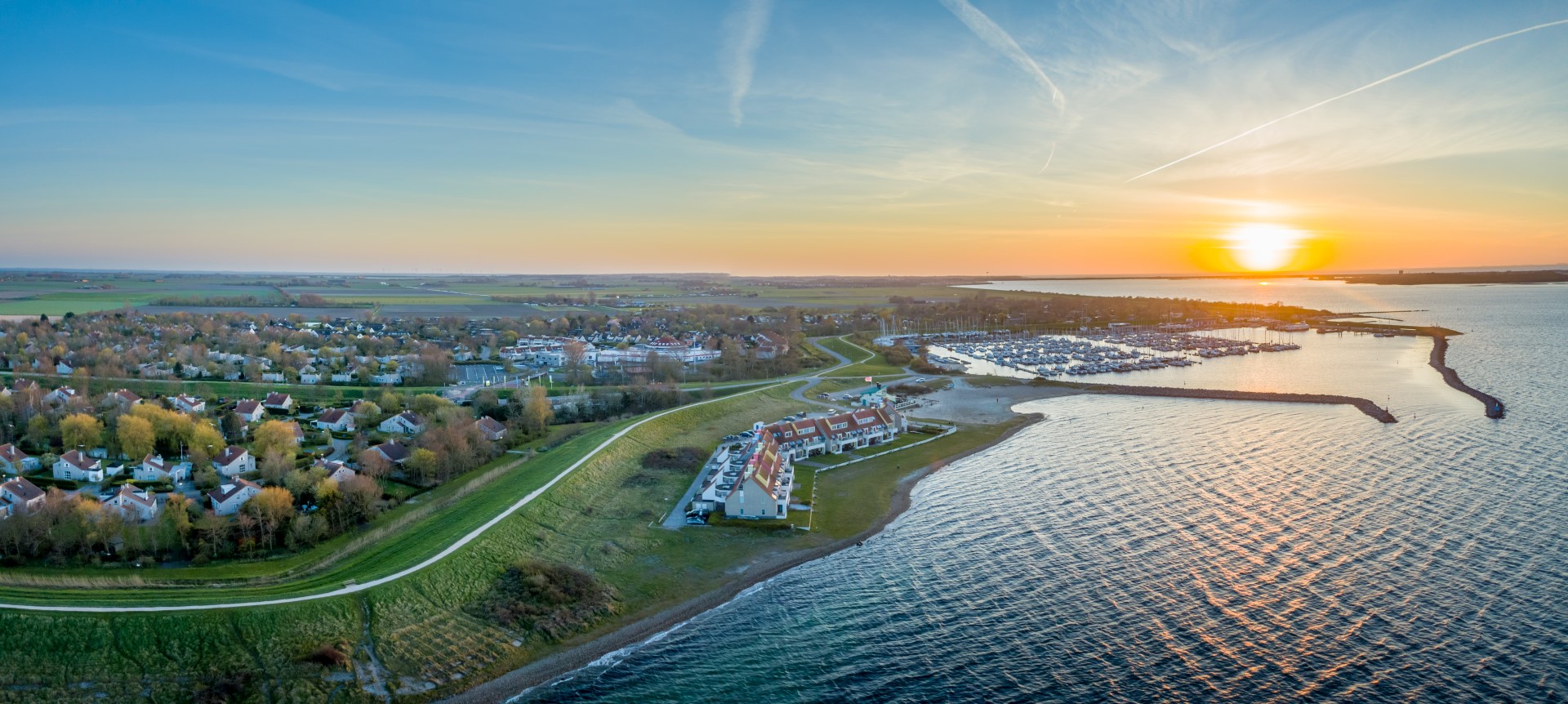 Panoramische luchtfoto van Vakantiepark Port Greve en de jachthaven tijdens een prachtige zonsondergang, met de vakantiehuizen aan het water.
