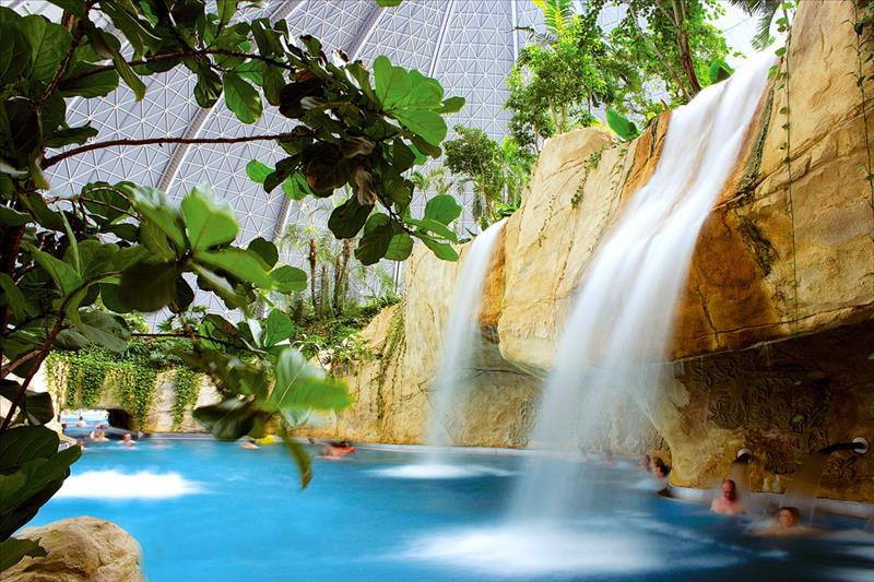 Een grote waterval stort in het helderblauwe water van de Bali Lagune, omringd door rotsen en tropische planten in de koepel van Tropical Islands.