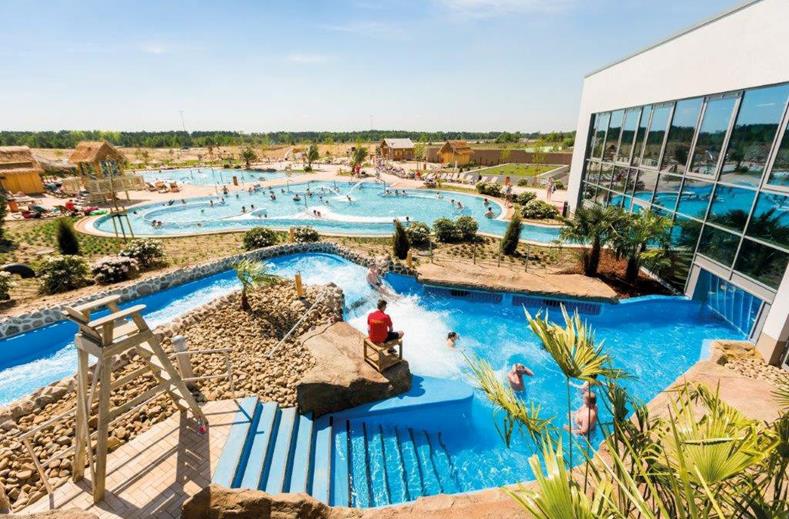 Bezoekers genieten van de zon en het water in het buitenzwembad AMAZONIA bij Tropical Islands, met de wildwaterbaan op de voorgrond.