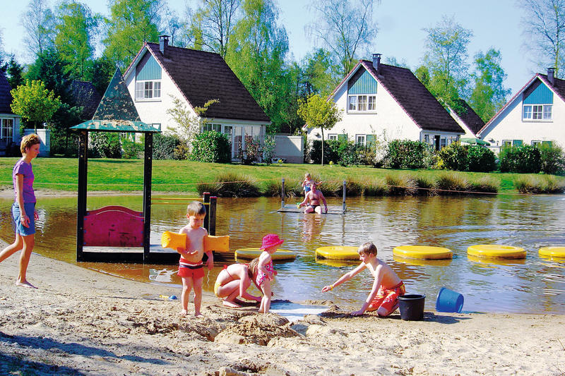 Kinderen bouwen zandkastelen op het strandje aan de recreatieplas van Vakantiepark Hellendoorn.