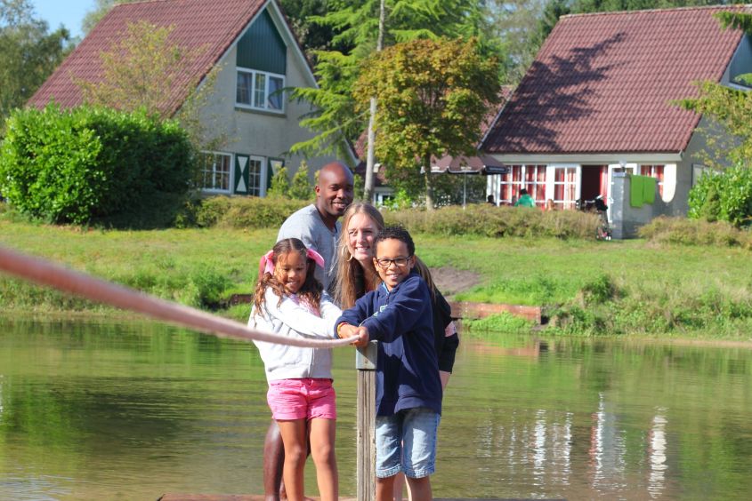 Een lachend gezin maakt gebruik van het trekvlot om de recreatieplas over te steken op Vakantiepark Hellendoorn.