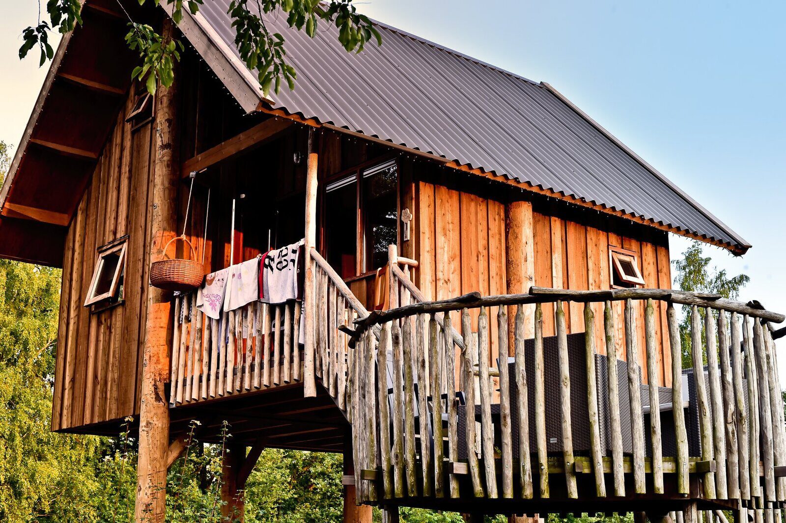De buitenkant van een luxe houten boomhut met een ruim terras, gelegen aan de rivier de Regge op Vakantiepark Molke.