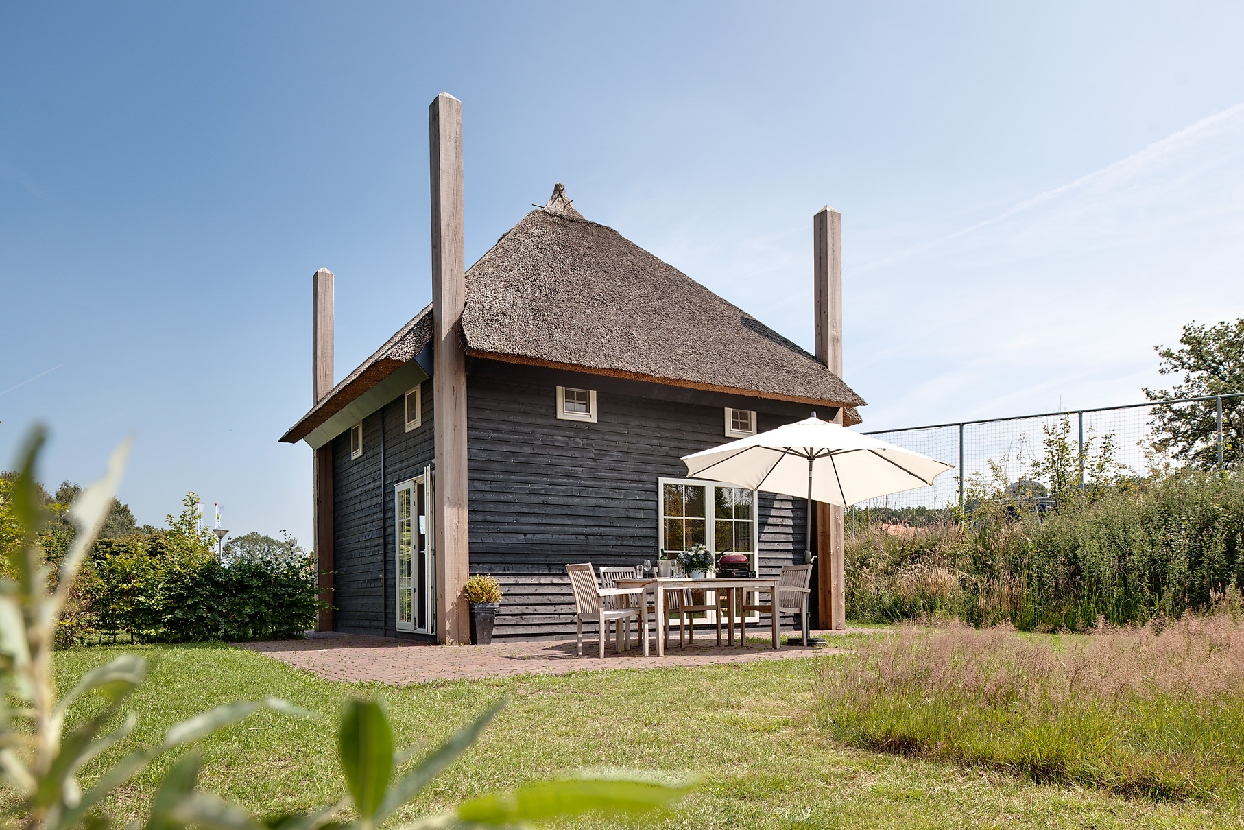 Een luxe, zwarte Regge Lodge met een rieten dak en een zonnig terras met tuinmeubilair op Vakantiepark Molke in Overijssel.