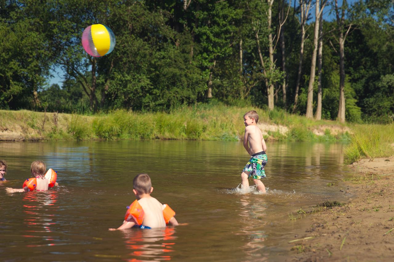 Twee jongens spelen met een bal in het ondiepe water van de rivier de Regge bij Vakantiepark Molke op een zonnige dag.