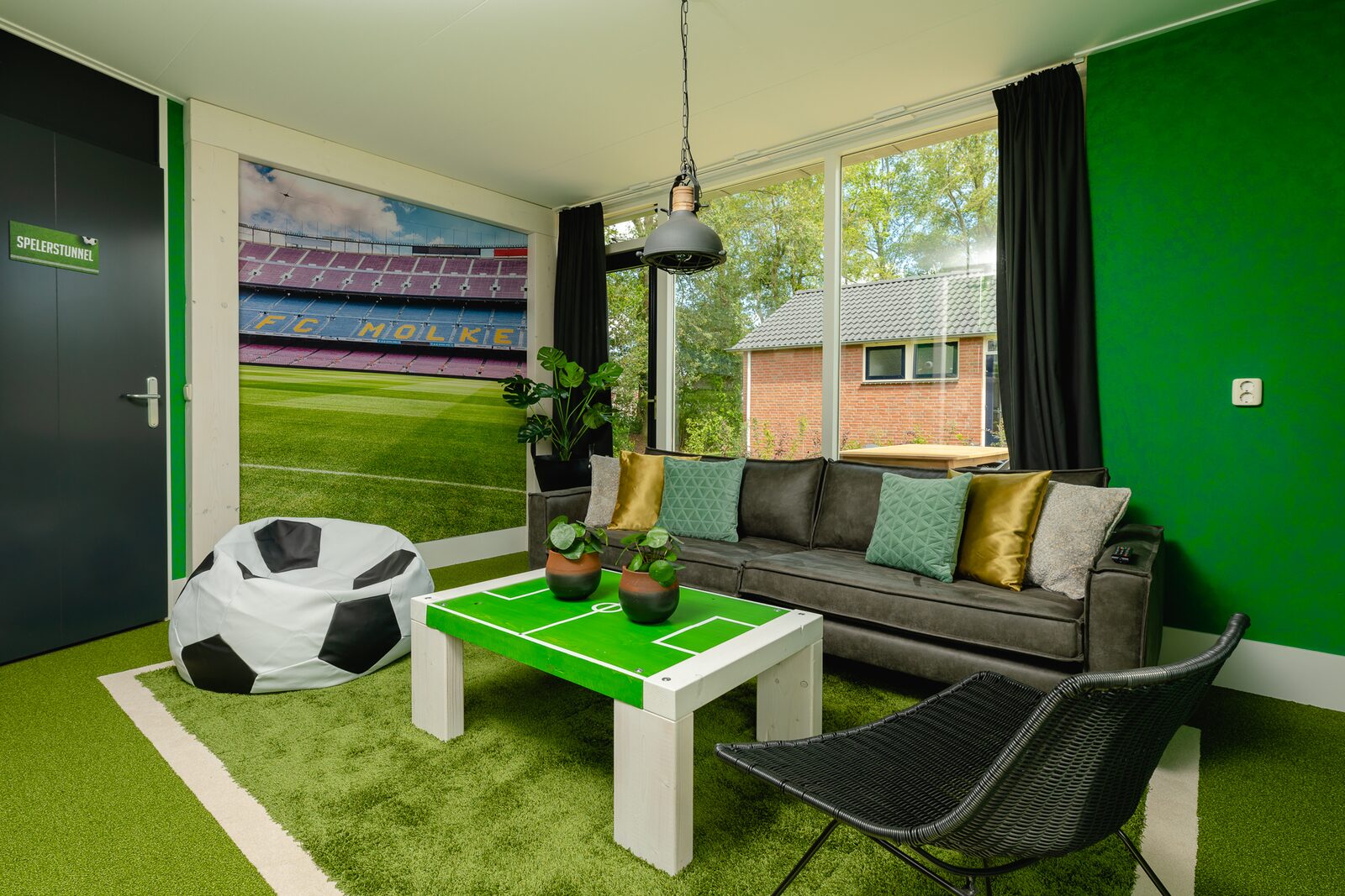 Het interieur van de Voetbal-lodge op Vakantiepark Molke, met een salontafel in de vorm van een voetbalveld en een zitzak als voetbal.