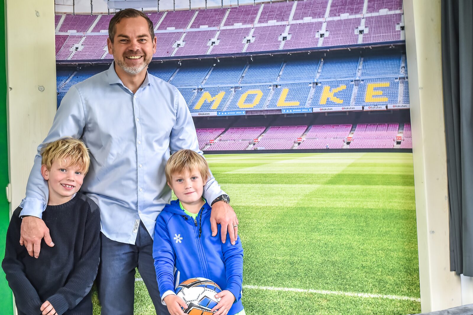 Een vader en zoon poseren voor de muur van een voetbalstadion-tribune in de speciale voetbal-lodge van Vakantiepark Molke.