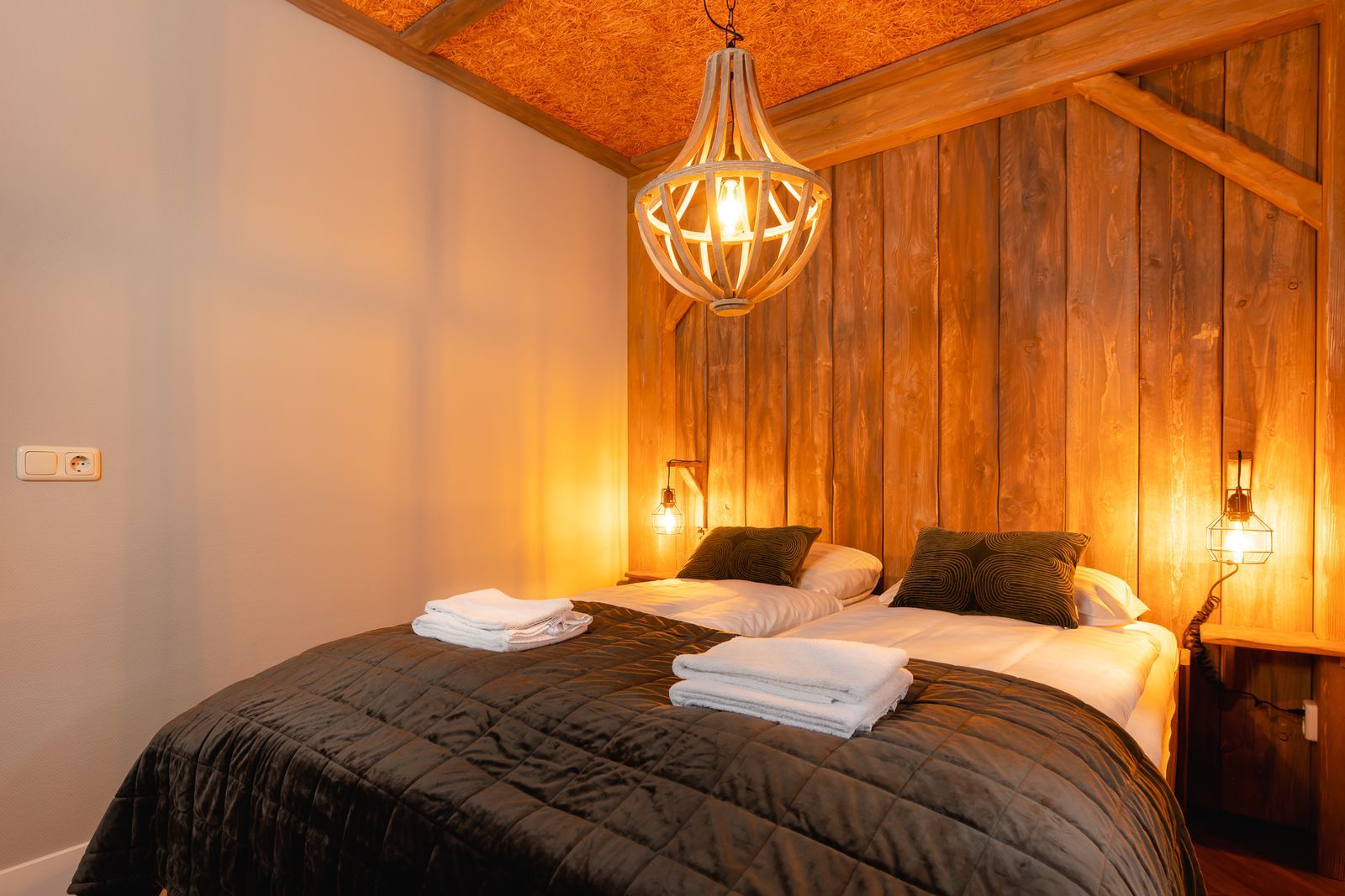 Een sfeervolle slaapkamer met opgemaakte bedden en een houten wand in een accommodatie op Vakantiepark Molke.