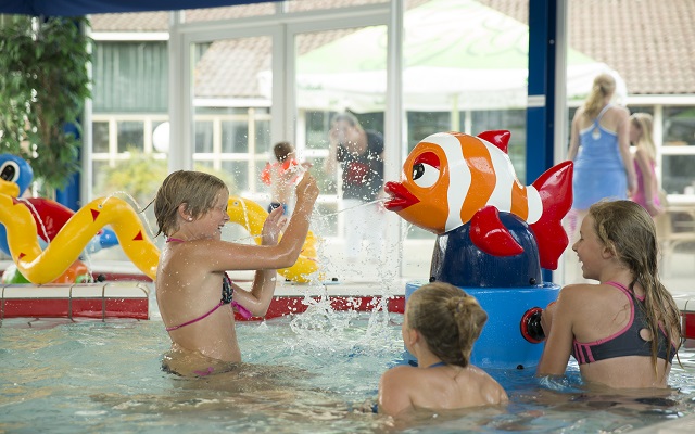 Kinderen spelen in het peuterbad van het binnenzwembad op Vakantiepark Molke, met een spuitend vis-speeltoestel.