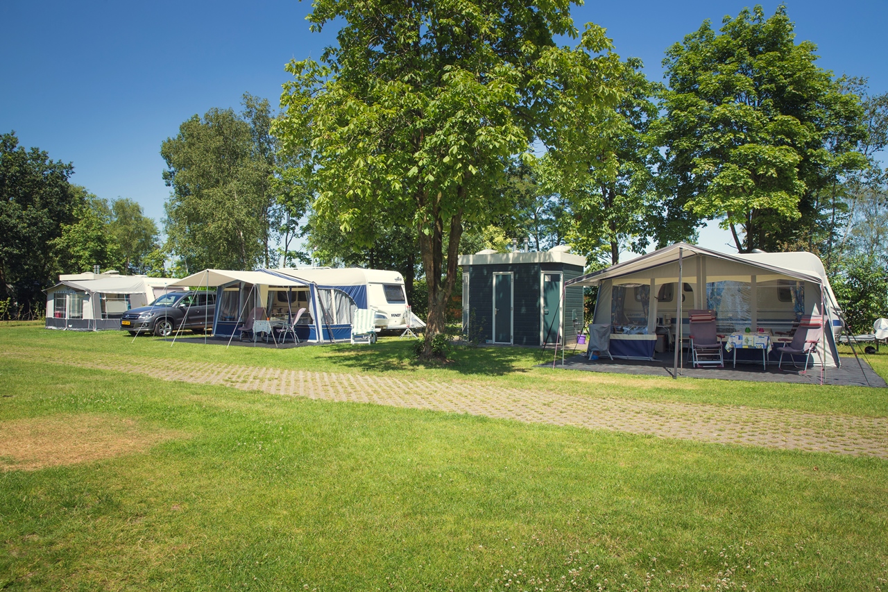 Een ruime, groene kampeerplaats met een caravan en voortent op de camping van Vakantiepark Molke in Overijssel.