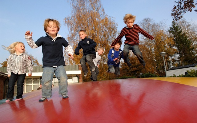 Een groep blije kinderen springt hoog in de lucht op de grote rode luchttrampoline van Vakantiepark Molke.