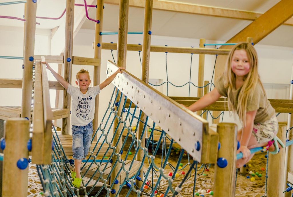 Kinderen klimmen over een touwbrug in de houten binnenspeeltuin van Vakantiepark Molke.