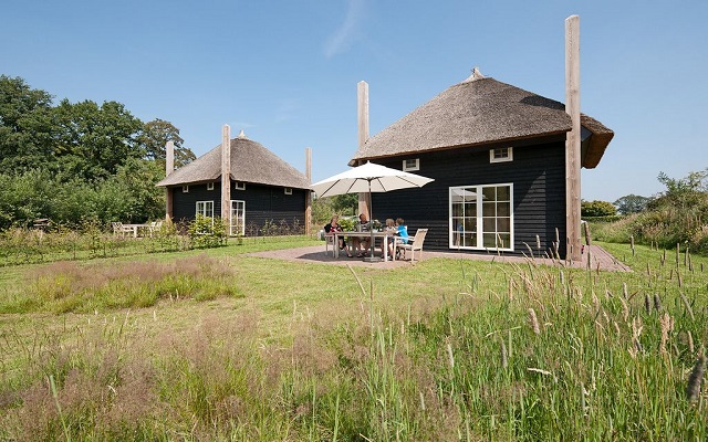 Twee luxe, zwarte Regge Lodges met rieten dak en een terras met een familie aan een tuintafel op Vakantiepark Molke.