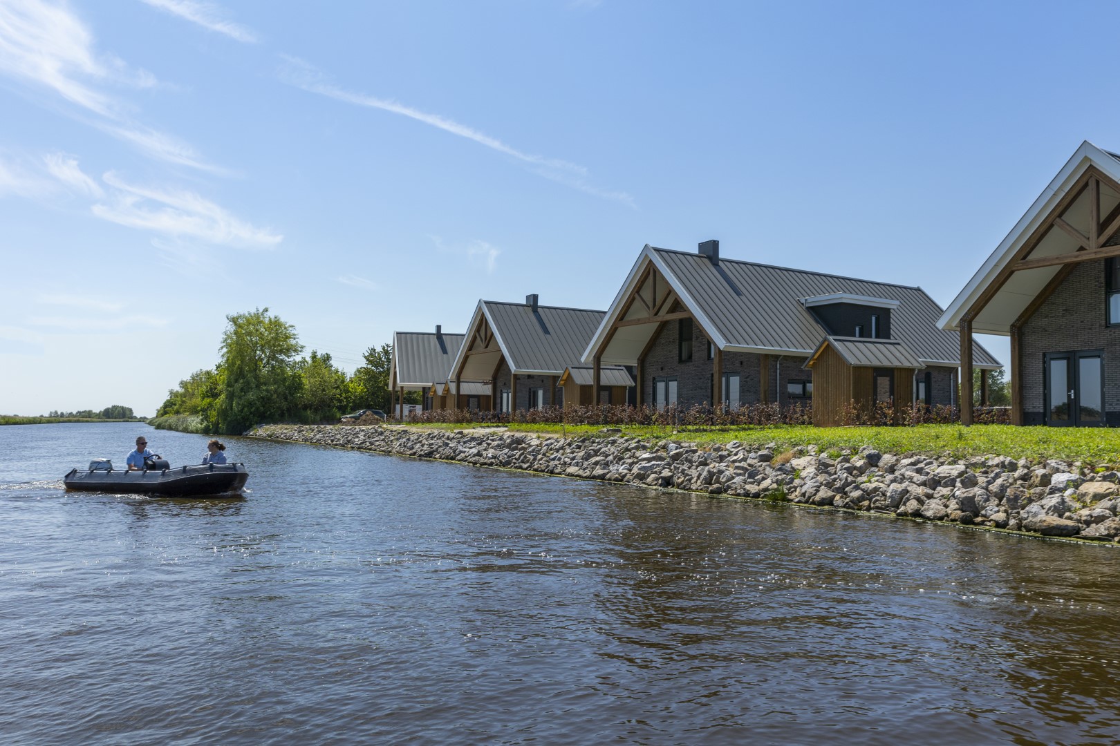 Een bootje met mensen vaart op een zonnige dag langs de moderne waterlodges van Waterpark Zwartkruis.