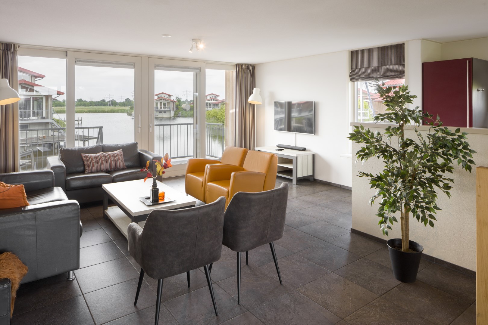 Stijlvolle woonkamer in een waterlodge op Waterpark Zwartkruis met grote ramen die direct uitzicht bieden op het water.